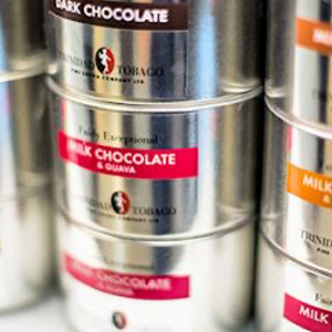 Close-up of stacked metal tins labelled with different flavours, featuring single-origin chocolate and fine flavour cocoa varieties like dark chocolate and milk chocolate with guava. | Trinitario