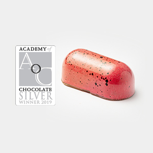 A pink and black speckled hand-crafted chocolate sits next to an Academy of Chocolate Silver Winner 2019 award badge. | Trinitario