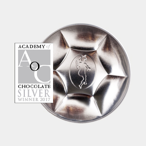 A round, silver, faceted handcrafted chocolate with an embossed goat logo, next to an "Academy of Chocolate Silver Winner 2017" badge. | Trinitario