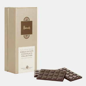 A beige Harrods chocolate box stands upright beside two dark chocolate bars, crafted from fine flavour cocoa, laid flat in front of it. | Trinitario