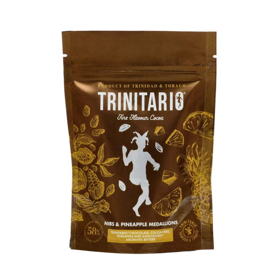 A brown pouch labelled “Trinitario Fine Flavour Cocoa” featuring gold illustrations of cocoa and pineapples, contains handcrafted chocolate nibs and pineapple medallions. | Trinitario
