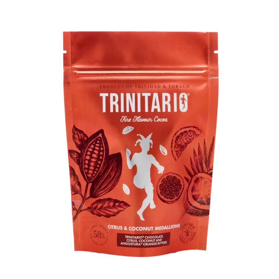 A red resealable pouch labelled "Trinitario Fine Flavour Cocoa" features cocoa pods, citrus fruits, and a dancing goat. The text highlights "Citrus & Coconut Medallions," handcrafted chocolate made with fine flavour cocoa. | Trinitario