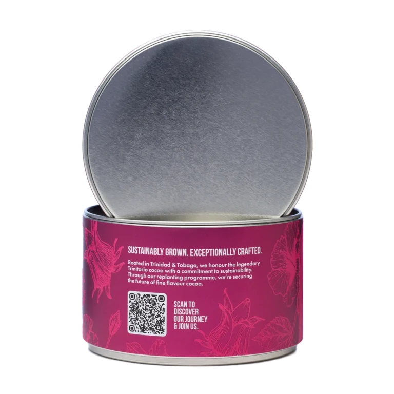 A round tin with a partially opened lid, featuring a pink label with floral patterns, text about sustainably grown chocolate, and a QR code for more information. | Trinitario