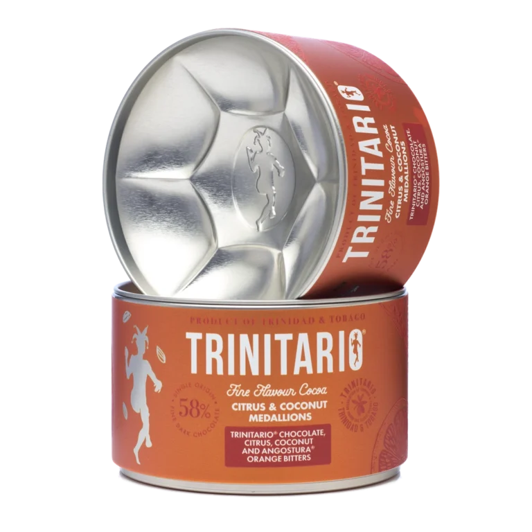 A round tin of single-origin chocolate Trinitario citrus and coconut medallions is shown, with the lid leaning against the container to display the logo and product details, highlighting its fine flavour cocoa origins. | Trinitario