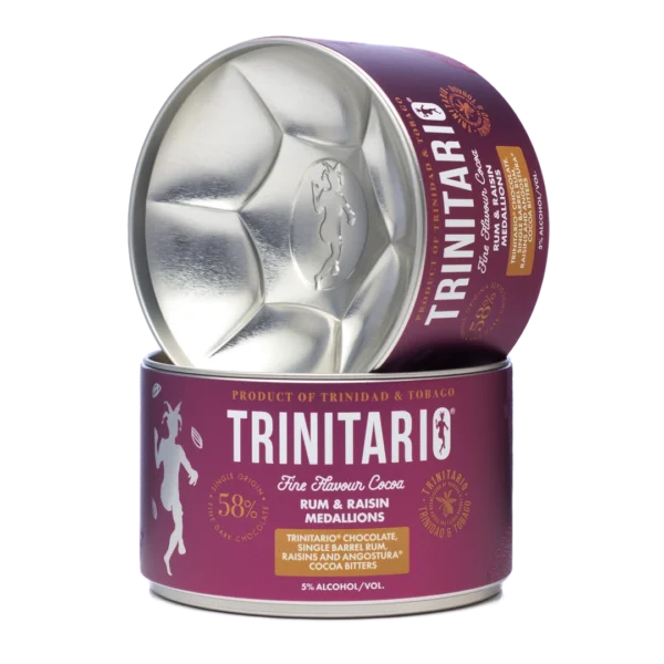 A round tin labelled "Trinitario Fine Flavour Cocoa" containing handcrafted rum and raisin chocolate medallions, with the lid leaning against the tin. | Trinitario