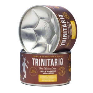 A canister of handcrafted Trinitario chocolate cocoa nibs and pineapple medallions, with the lid resting upright beside the open container, showing the metallic interior. | Trinitario