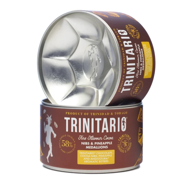 A canister of handcrafted Trinitario chocolate cocoa nibs and pineapple medallions, with the lid resting upright beside the open container, showing the metallic interior. | Trinitario
