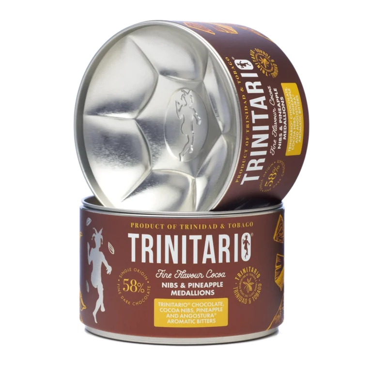 A canister of handcrafted Trinitario chocolate cocoa nibs and pineapple medallions, with the lid resting upright beside the open container, showing the metallic interior. | Trinitario