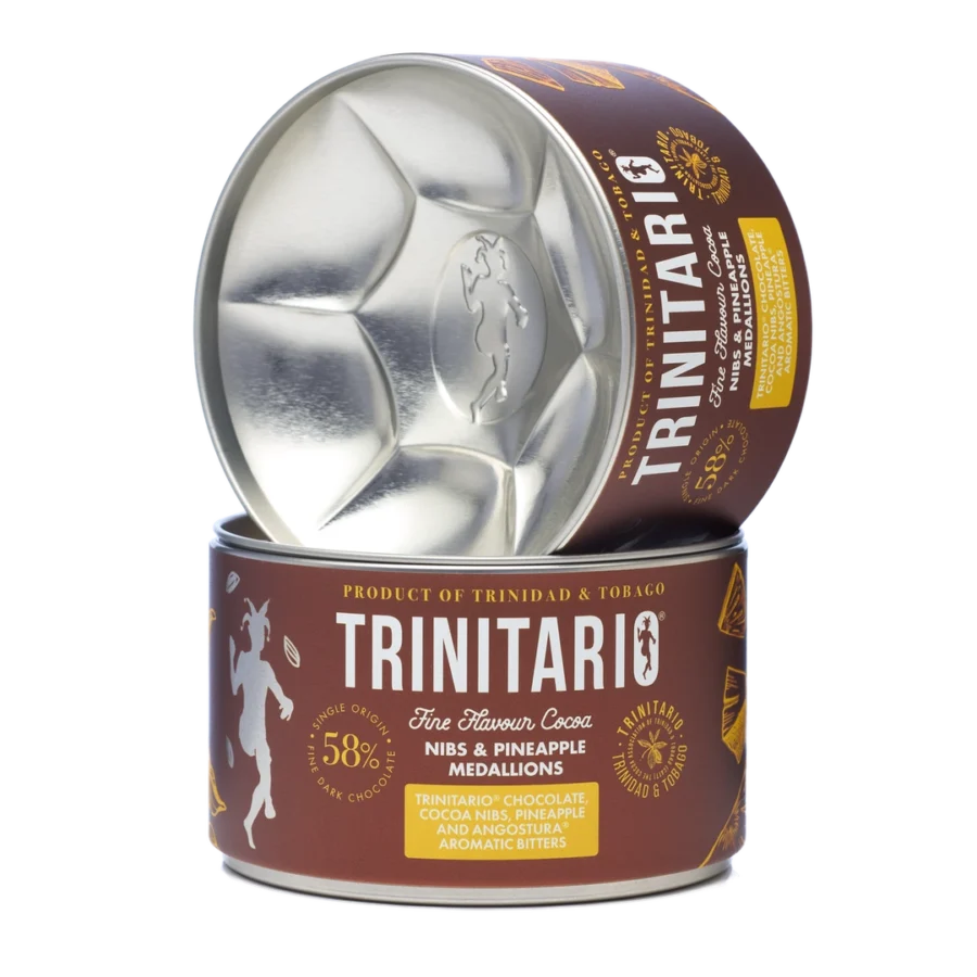 A canister of handcrafted Trinitario chocolate cocoa nibs and pineapple medallions, with the lid resting upright beside the open container, showing the metallic interior. | Trinitario