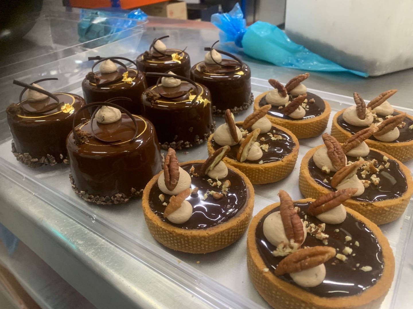 Two types of chocolate desserts on a tray: round glossy cakes made with single-origin chocolate, and tarts topped with pecans, cream, and rich chocolate glaze. | Trinitario
