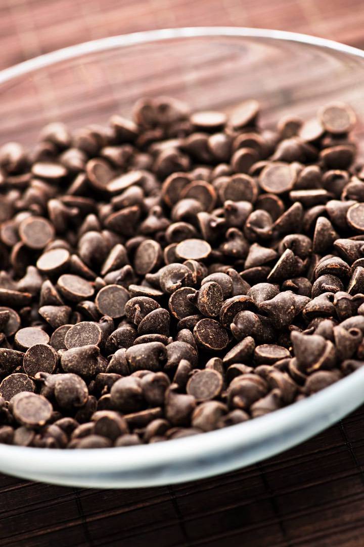 A clear glass bowl filled with semi-sweet chocolate chips made from fine flavour cocoa sits on a brown woven surface. | Trinitario