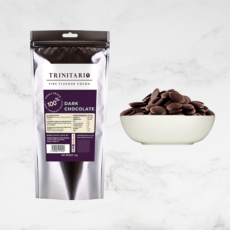 A silver package labelled "100% Dark Chocolate Callets, 1kg" stands beside a white bowl filled with hand-crafted chocolate callets on a light background. | Trinitario