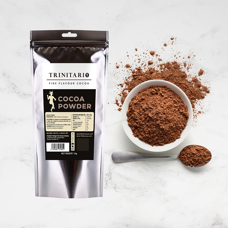 A silver pouch labelled "Cocoa Powder, 1kg," made from sustainably grown chocolate, sits next to a white bowl and spoon filled with cocoa powder on a white marble surface. | Trinitario