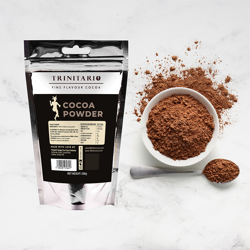 A 200g pouch of Cocoa Powder sits beside a white bowl and a spoon filled with cocoa powder, some scattered on the surface—perfect for making rich, hand-crafted chocolate treats. | Trinitario