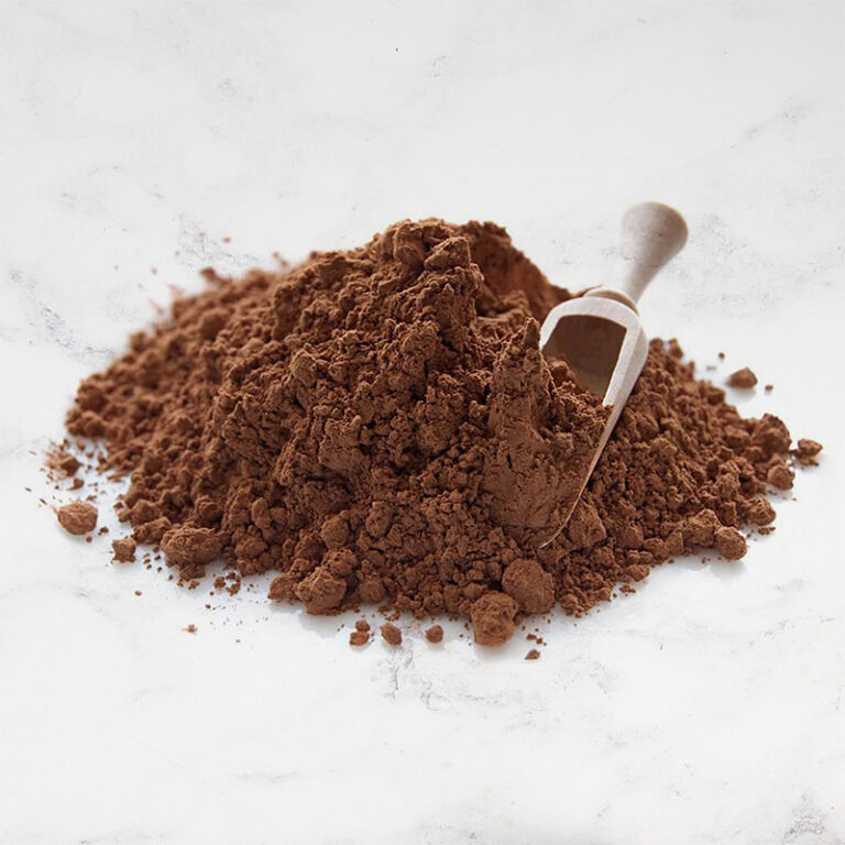 A wooden scoop rests in a pile of Cocoa Powder, 25kg, displayed on a white surface. | Trinitario