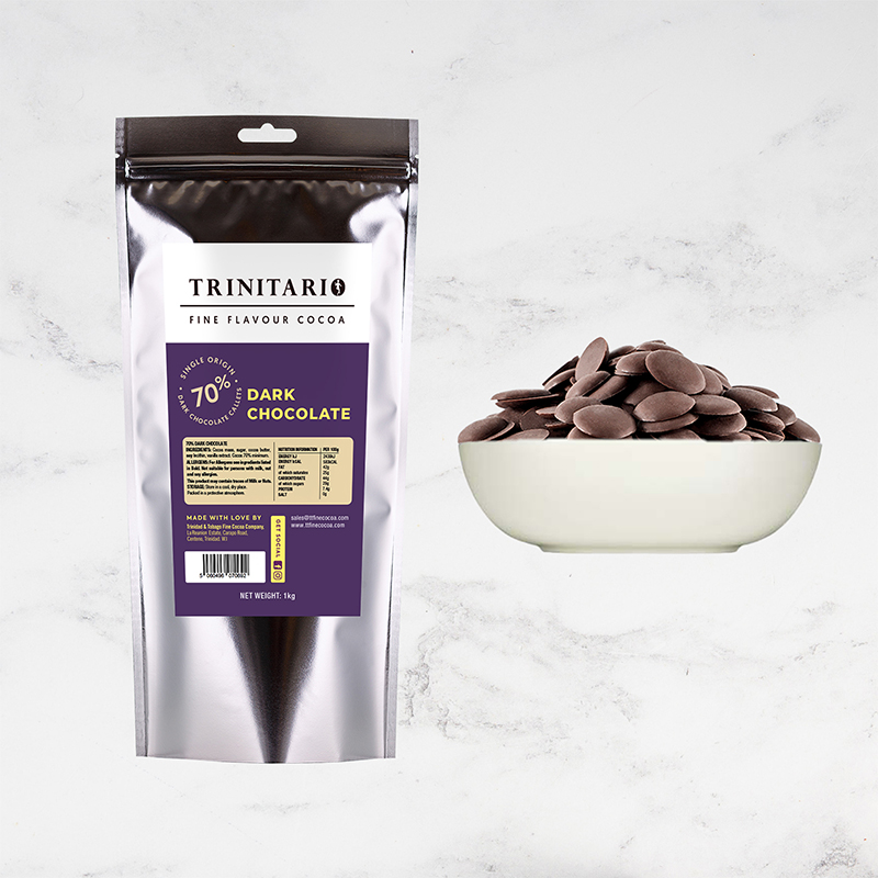 A silver packet labelled "70% Dark Chocolate Callets, 1kg" sits next to a white bowl filled with dark chocolate discs, highlighting premium Caribbean single-origin chocolate on a light marble surface. | Trinitario