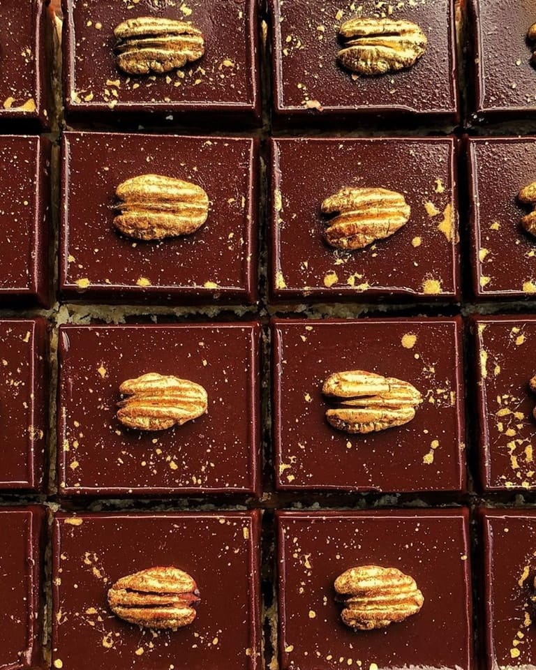 Rows of hand-crafted chocolate desserts, made with single-origin chocolate, are topped with pecan halves and gold splatter decoration. | Trinitario