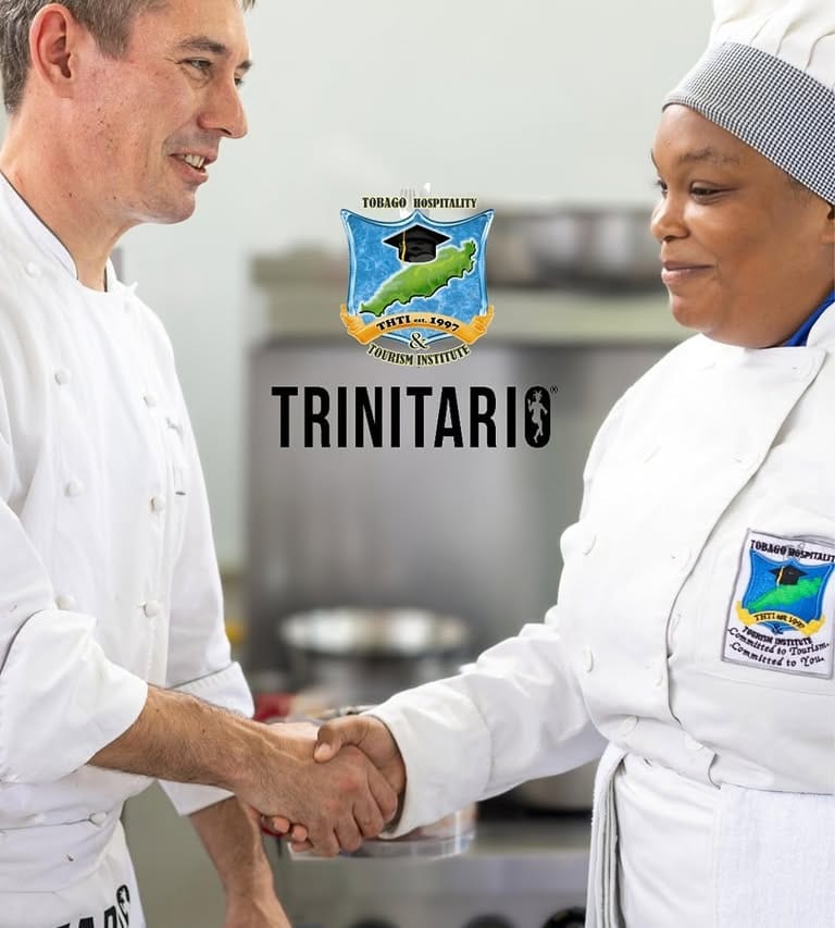 Two chefs in Tobago Hospitality & Tourism Institute uniforms shake hands in a professional kitchen. The word "TRINITARIO" and the institute crest highlight their expertise in single-origin Trinitario chocolate. | Trinitario